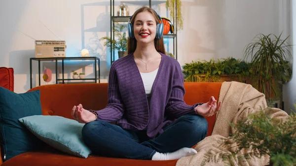 Keep calm down, relax, inner balance. Portrait of woman breathes deeply with mudra gesture, eyes closed, meditating with concentrated thoughts, peaceful mind at home apartment. Girl sitting on couch