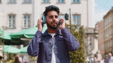 Kablosuz kulaklıklı, neşeli, neşeli genç Hintli adam dışarıda akıllı telefon dansında en sevilen disko rock 'n roll müziğini dinliyor. Şehir caddesinde yürüyen turist.