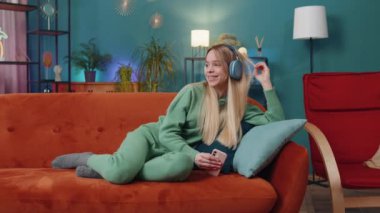 Kablosuz kulaklıklı, evinde koltuğa uzanmış, en sevilen disko müziği dinleyen mutlu beyaz kadın. İnsanlar hafta sonu boş zaman aktiviteleri
