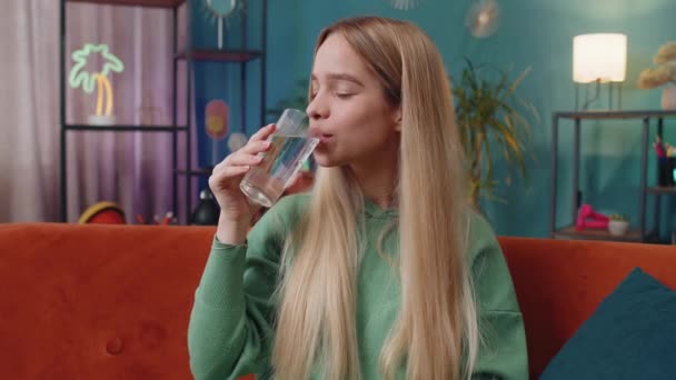 口渴的女人拿着一杯天然水 让小口小口喝水 防止脱水 坐在家里客厅里 白人女孩 生活习惯好 体形降 体重减轻观念 — 图库视频影像