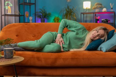 Adet sancısı çeken hasta bir kadın. Oturma odasındaki kanepede yatarken karın ağrısı çekiyor. Karnını tutan bir kız, karın ağrısı ya da regl ağrısı çekiyor. Karın ağrısı, mide iltihabı, ishal, hazımsızlık.