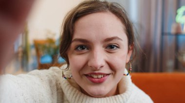 İnternetten selfie çeken, el sallayan, evde otururken kameraya bakan genç bir kadının görüntüsü. İletişim, toplantı. Esmer kız blogcu akıllı telefon konuşması yapıyor