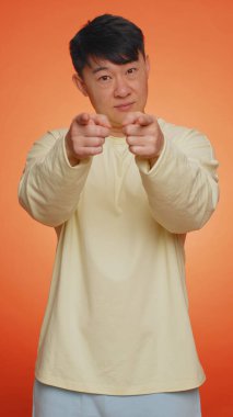 Seni seçiyorum. Asyalı bir adam kamerayı işaret ediyor ve neşeli bir ifadeyle bakıyor, seçim yapıyor, yön gösteriyor, iş yerinde eleman arıyor. Turuncu arka plandaki adam. İnsanların yaşam tarzları. Dikey