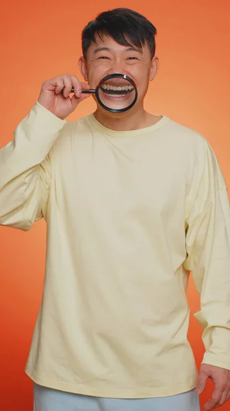 Азиатский Мужчина Держащий Увеличительное Стекло Здоровых Белых Зубах Смотрящий Камеру — стоковое фото