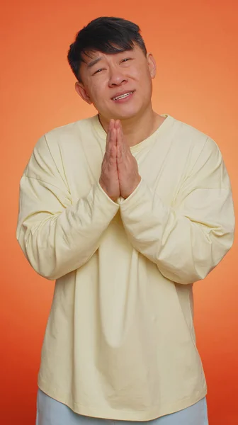 助けてくれ許してくれないか アジアの男は祈り 上を向いて願い事をし 希望に満ちた表情で祈り 謝罪を請う オレンジの背景に隔離された中国人 — ストック写真