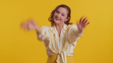 Buraya gel, bize katıl. Hoş geldiniz. Esmer, çekici bir kadın elleriyle davetkar bir jest yapıyor. Katılmak istiyor. Gelmeye çağırıyor. Sarı stüdyo arka planında izole güzel bir kız.