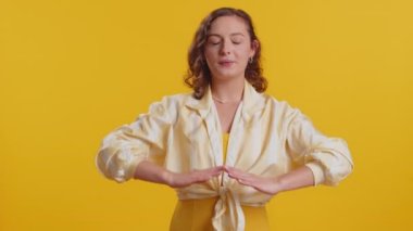Sakin ol, rahatla, iç denge. Genç kadın derin nefes alıyor Mudra jesti, gözleri kapalı, konsantre düşüncelerle meditasyon yapıyor, huzurlu bir zihin. Sarı arka planda izole edilmiş çekici bir kız.