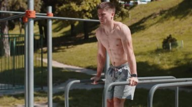 Atletik beyaz üstsüz kaslı adam karın kaslarını çalıştırıyor, paralel barlarda abdominal mekik çekiyor. Oyun parkındaki tişörtsüz adam. Spor, sağlık, spor, spor, jimnastik. Motivasyon