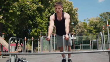 Spor giyimli beyaz kaslı bir adam oyun parkında şınav çekiyor. Tişörtlü genç vücutçu. Spor, sağlık, spor, spor, spor. Güç, motivasyon. Açık hava spor salonu
