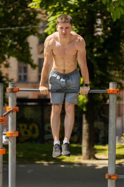 stock image Athletic caucasian topless muscular training force push up, pull up exercise, strength gymnastics elements on horizontal bar. Young shirtless guy on playground. Sports health fitness routine, workout