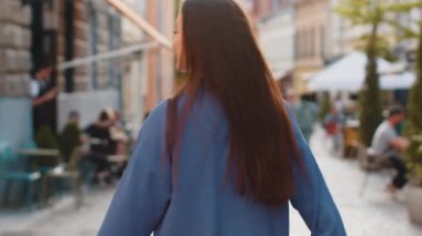 Avrupa sokaklarında gezen mutlu genç kadın turistin arkası dönüp kameraya bakıyor. Şehir arka planında gezen güzel bir kız gezginin arka görüntüsü. Kasaba yaşam tarzları