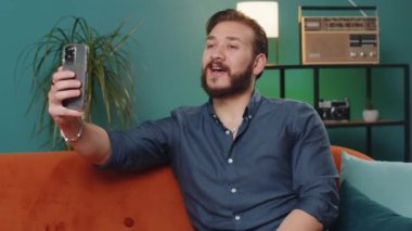 Lübnanlı mutlu blogcu akıllı telefondan selfie çekiyor, sosyal medya takipçileriyle çevrimiçi video görüşmesi yapıyor, vlog hikayeleri kaydediyor. Evdeki kanepede oturan genç bir Arap.