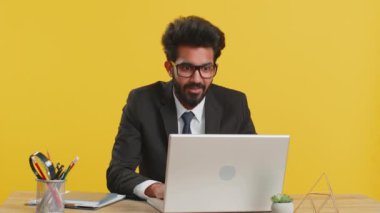 Heyecanlı Hintli iş adamının kafasına dokunması, patlamayı göstermesi, endişeli görünmesi, iş yerindeki profesyonel yorgunluk. Resmi takım elbiseli Hindu adam sarı arka planda dizüstü bilgisayarda çalışıyor.