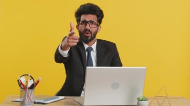 Hey sen! Hintli işadamı heyecanlı bir şekilde gülümsüyor ve kamerayı işaret ediyor, şanslı kazananı seçiyor, ofis çalışma masasına işaret ediyor. Resmi takım elbiseli Hindu, sarı arka planda izole edilmiş dizüstü bilgisayarla çalışıyor.