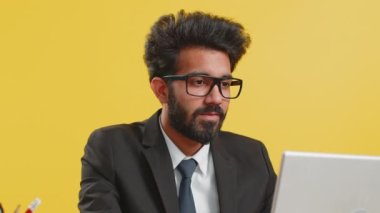 İş yerindeki Hintli iş adamı, sarı arka planda izole edilmiş dizüstü bilgisayarla çalışıyor. Müdür Hindu serbest çalışan adam defter üzerinde çalışıyor mesajlar gönderiyor çevrimiçi alışverişler yapıyor