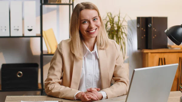 照片上 现代总公司工作间的年轻女商人面带微笑地看着相机 脸上洋溢着快乐的笑容 身着正式服装的女性 漂亮可爱的女人在笔记本电脑上远程在线工作 — 图库照片