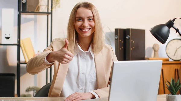 快乐的年轻女商人在笔记本电脑上工作时 赞许地看着展示大拇指的相机 喜欢在办公室的办公桌上签积极正面的东西 积极的反馈 自由职业者的女人 — 图库照片