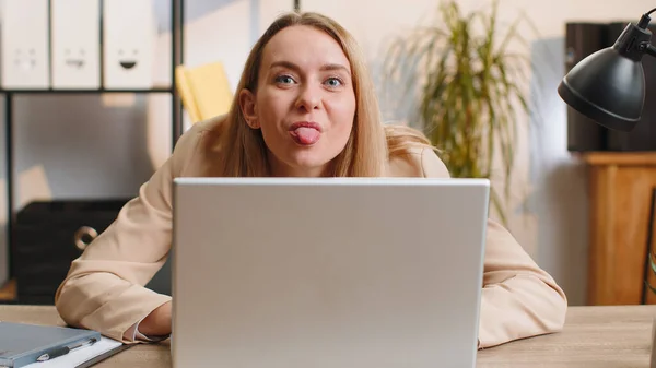 年轻的女商人躲在笔记本电脑后面做鬼脸 把舌头伸出去远程办公 不尊重办公室里的某个人 自由职业妇女 — 图库照片