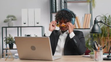 Mutlu, aşırı mutlu Hintli iş adamı ev bilgisayarında çalışıyor kulaklık takıyor ve en sevilen enerjik disko müziğini dinliyor ve dans ediyor. Serbest çalışan adam dinleniyor, mola veriyor.