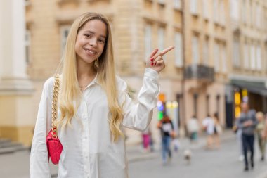 Mutlu genç bir kadın reklam için boş bir yeri işaret ediyor. Ticari metin fotokopi alanı ürün tanıtımı için. Kız turist çözüm düşünüyor, ilham kaynağı şehir sokaklarında hayaller kuruyor.