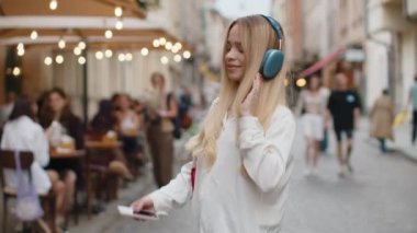 Kablosuz kulaklıklı, neşeli, neşeli genç bir kadın dışarıda dans ederken en sevilen disko rock 'n roll müziğini dinliyor. Şehir caddesinde yürüyen genç kız