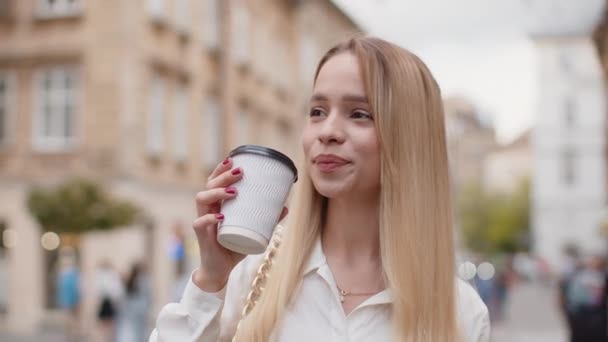 아침에 커피를 즐기고 밖에서 미소짓는 금발의 도시의 거리를 소녀가 커피를 — 비디오