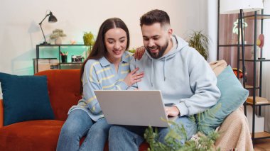 Aşırı mutlu aile evliliği erkek kadın dizüstü bilgisayar kullanarak büyük ikramiyeyi kutluyor. Şanslı galibiyet, oyun oynama, internetten alışveriş. Karı koca kanepede yan yana.