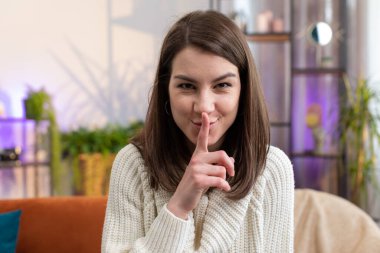 Sessiz olun lütfen, sessiz olun. Genç bir kadının portresi işaret parmağını dudaklarına bastırıyor. Sessiz ol işareti yapıyor. Ev odasında dedikodu sırrını kimseye söyleme. Güzel kız kanepede oturuyor.