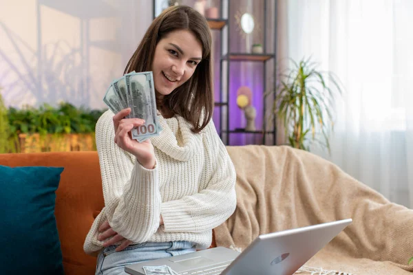 Planning budget. Rich happy young woman counting money cash use laptop computer calculate domestic bills at home apartment. Girl satisfied of income earnings, saves money for planned vacation, gifts