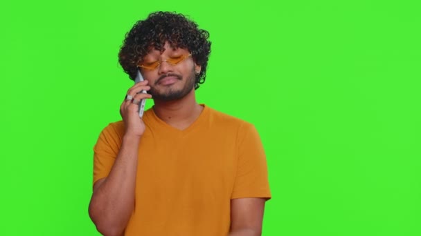 スマートフォンで退屈な話をしていた若いインド人の興味をそそりません 疲れて眠いHindu男は友人と携帯電話で話して 緑のクロマキーの背景に隔離されたオンライン会話を作る — ストック動画