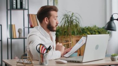 Ofis masasında dizüstü bilgisayarda çalışan bir iş adamı çalışanla online iletişim videosu konuşması yapıyor, patron grafik analizi gösteriyor. Bilgisayarın webcam görüntülerine bakan yönetici destek servisleri