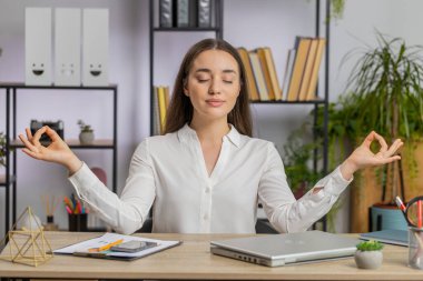 Kafkasyalı iş kadını dizüstü bilgisayarda çalışıyor, yoga solunum egzersizi yapıyor ev ofisinde lotus pozisyonunda. Sakin, serbest çalışan bir kız mola veriyor. Meşgul bir iş. İç huzuru