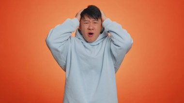 Handsome asian man feeling hopelessness loneliness, nervous breakdown, loses becoming surprised by lottery results, bad fortune, loss, unlucky news. Chinese guy isolated on studio orange background