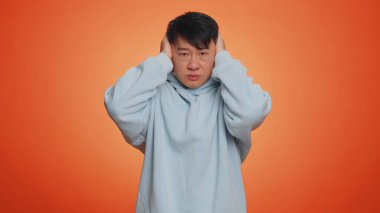 Dont want to hear and listen. Frustrated annoyed irritated asian man covering ears gesturing No, avoiding advice ignoring unpleasant noise loud voices. Handsome chinese guy alone on orange background