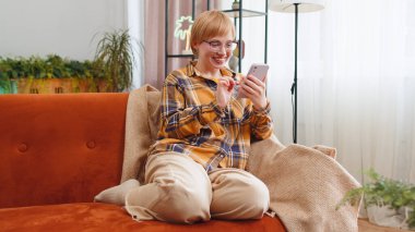 Kanepede oturan genç bir kadının portresi evde gülümseyen bir cep telefonu kullanıyor. Akıllı telefon sosyal medya uygulamaları üzerinden rahatlama filmi izlerken mesajları paylaşan kız