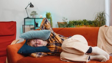 Repair work at neighbours. Irritated woman girl relaxing on couch cover ears with pillows annoyed by noisy neighbors suffer from headache wish silence. Thin walls at home flat without sound insulation