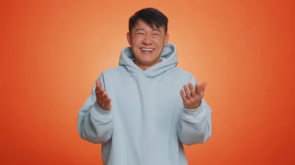 有名なアジアの男のカメラに指を指して 大声で笑い ばかばかしい外観 面白い冗談の逸話の楽しさを試飲 ハンサムな中国人男絶縁一人でオレンジ色のスタジオの背景 — ストック写真