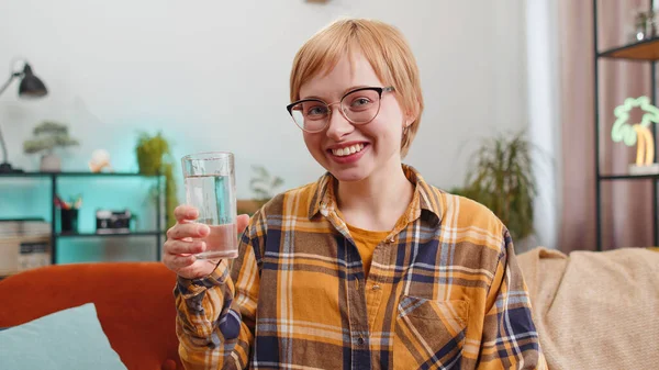 口渴的年轻女子拿着一杯天然水 让小口小口喝水 防止脱水 坐在家里的客厅里 具有良好生活习惯 健康体形 体重减轻观念的女孩 — 图库照片