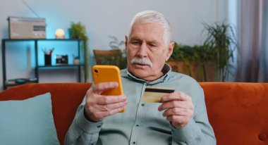 Büyükbaba kredi kartı ve akıllı telefon kullanarak para transfer ediyor, internetten nakit para almıyor, yemek siparişi veriyor, ev içinde faturaları ödüyor. Kanepedeki yaşlı adam.