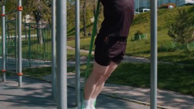 Spor giyimli atletik bir adam elastik genişleticinin yardımıyla barfiks egzersizi yapıyor. Çocuk parkında sırt kaslarını şişiren genç adam. Spor sağlığı rutin egzersizi. Vücut geliştirme