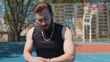 Lübnanlı atletik koşucu spor giyim kuşamında akıllı saat kullanıyor, kalp atışlarını kontrol ediyor, koşma rotasını kontrol ediyor. Basketbol sahasındaki genç adam maçtan önce ısınıyor. Spor, spor rutini, egzersiz.