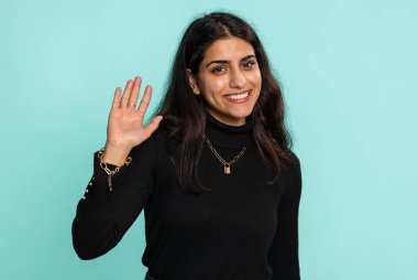 Buraya gel, bize katıl. Hoş geldiniz. Hindu Arap kadın elleriyle davetkar bir jest yapıyor, katılmak istiyor, gelmek için işaret ediyor, merhaba diyor, güle güle. Mavi stüdyo arka planında izole edilmiş güzel Hintli kız.