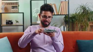 Neşeli, mutlu, zengin Hintli adam israf gösteriyor, el hareketleriyle etrafa para saçıyor, daha fazla bahşiş veriyor, daha fazla kazanç sağlıyor, piyango kazanıyor, vücut dili kazanıyor, paylaşıyor, kutluyor. Oturma odasındaki adam.