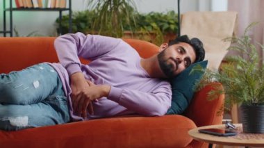 Genç Hintli adam kanepeye uzanmış karın ağrısı ve mide iltihabı şikayeti yaşıyor. Hindu adam ishal, hazımsızlık, peptik ülser pankreatiti geçiriyor.