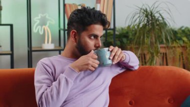 Çekici, gülümseyen Hintli adam sabahları bir fincan sıcak kahve ya da bitki çayı içiyor. Hintli adamın portresi turuncu kanepede evde tek başına rahatça oturup rahatlıyor.