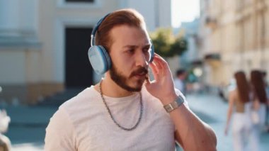 Kablosuz kulaklıklı, neşeli sakallı mutlu genç adam dışarıda dans eden enerjik disko rock 'n roll müziğini dinliyor. Şehir Güneşi Sokağı arka planında yürüyen adam