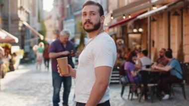 Mutlu sakallı genç adam sabah kahvesinin tadını çıkarıyor sıcak içecek ve dışarıda gülümsüyor. Dinleniyorum, ara veriyorum. Şehirdeki Sunshine Caddesi 'nde yürüyen ve kahve içen bir adam. Dışarıdaki kasaba yaşam tarzları