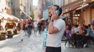 Kablosuz kulaklıklı, neşeli, neşeli genç bir adam dışarıda dans ederken en sevilen disko rock 'n roll müziğini dinliyor. Şehir merkezinde yürüyen adam.