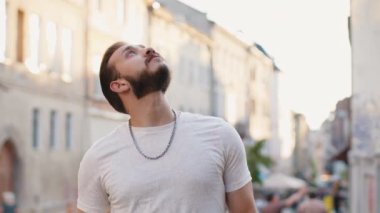 Sakallı genç bir turistin portresi. Şehir sokaklarında yaz güneşli bir günde yürüyor. Gezgin adam gülümsüyor ve dışarıda eğleniyor. Kasaba yaşam tarzları, tatil