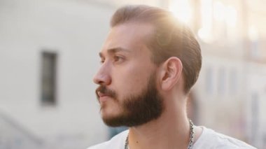 Mutlu genç adamın yakın plan portresi gülümseyen arkadaş canlısı, mutlu gözler kameraya bakıp dinlenen rahatlama hayalleri kuran açık havada iyi haberler veriyor. Güneşli şehir sokağındaki sakallı adam.